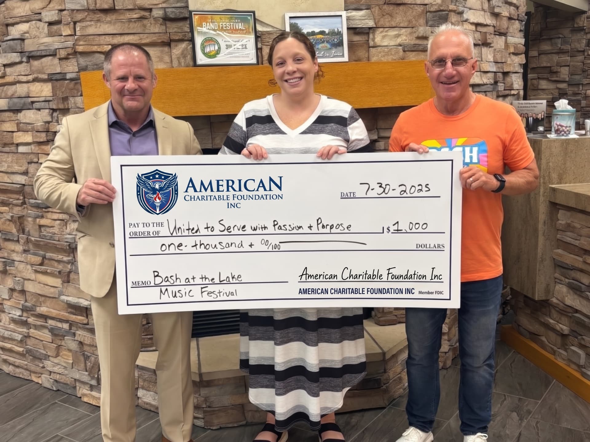 Three people presenting a large ACF grant check for United to Serve with Passion and Purpose in a lounge with a stone fireplace