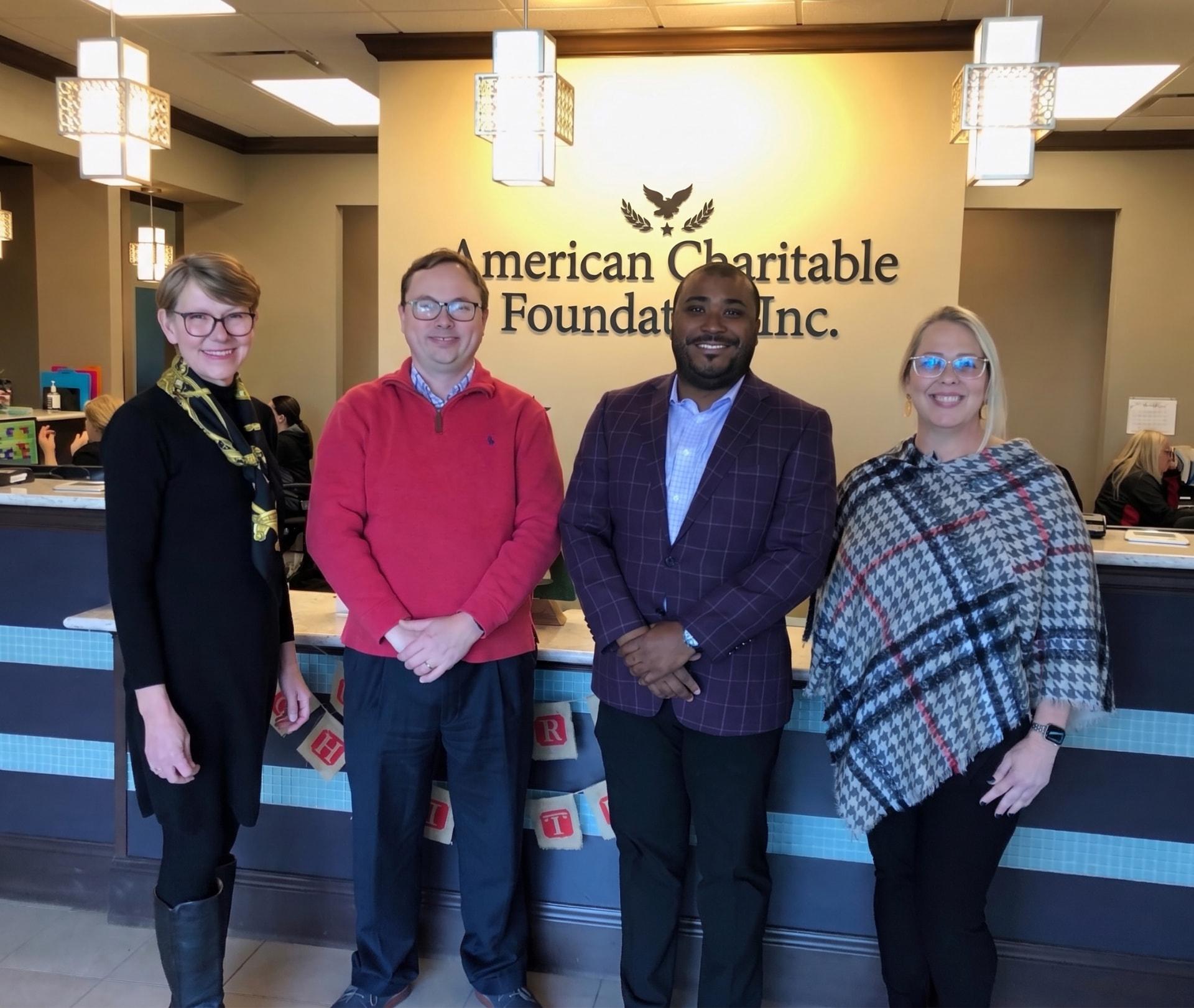 A group of ACF representatives standing together at the front desk beneath the American Charitable Foundation Inc. sign