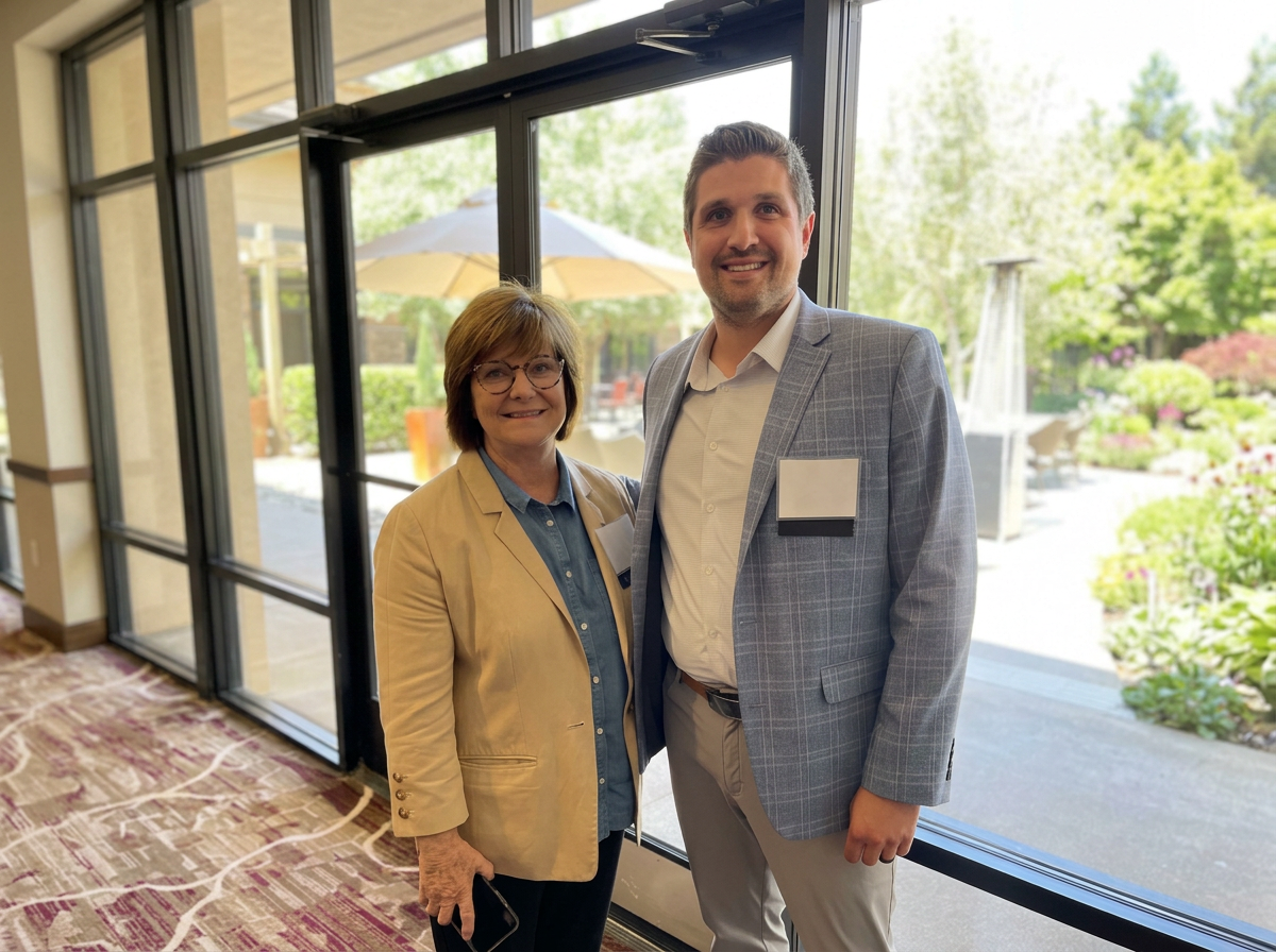 Two ACQA representatives smiling beside windows with a garden view