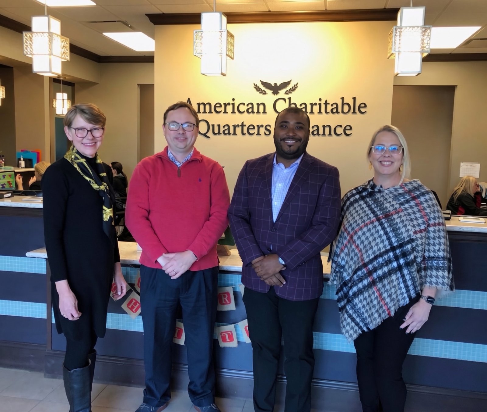 A group of ACQA representatives standing together at the front desk beneath the ACQA sign